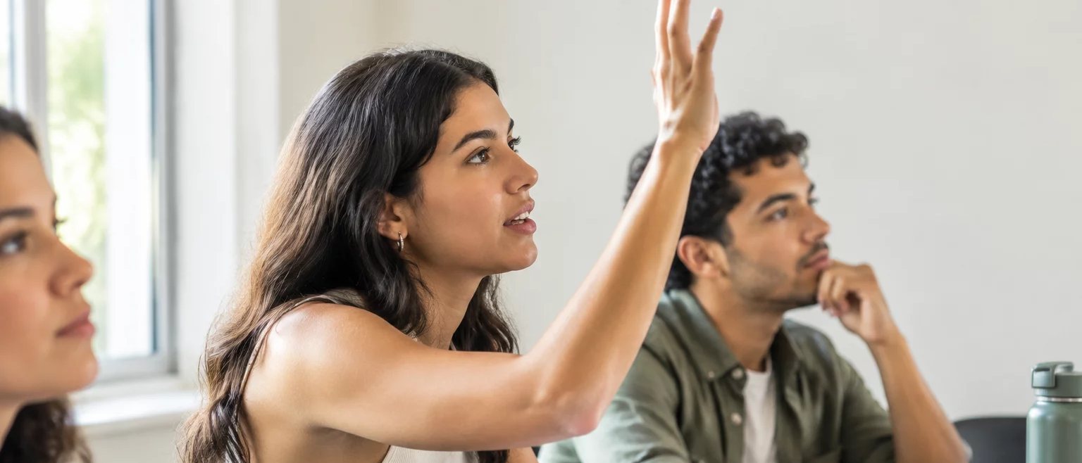 Participante com a mão erguida pedindo a vez, à mesa coberta de folhas escritas